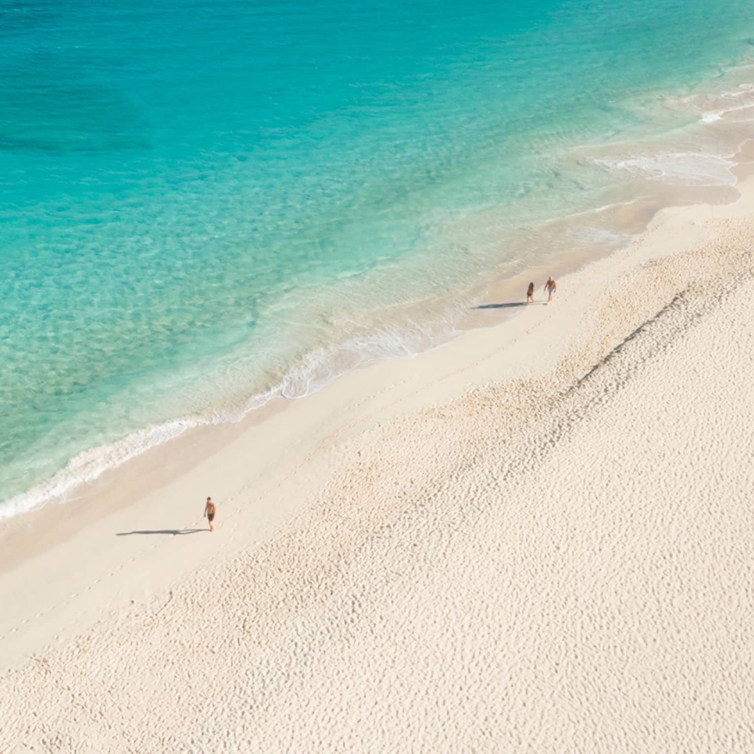 Aerial view of people walking on a white sandy beach beside crystal clear, blue waters