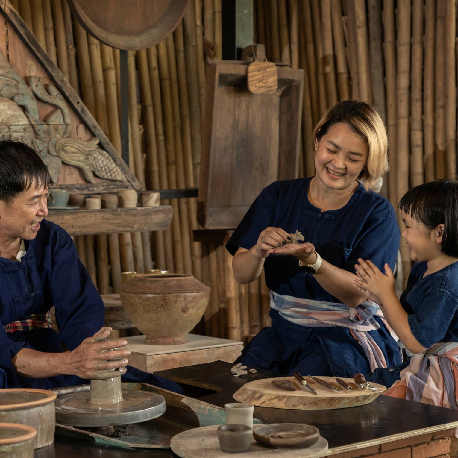 A potter teaching a woman and a child to shape clay in a rustic pottery workshop, surrounded by traditional tools and pottery.