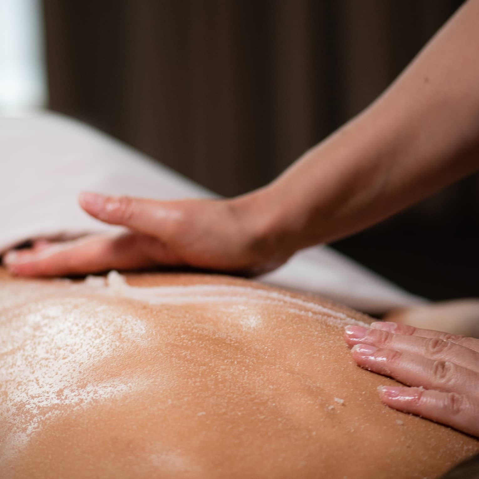 A masseuse spreads a cream across a woman's back as she lies on a massage table.