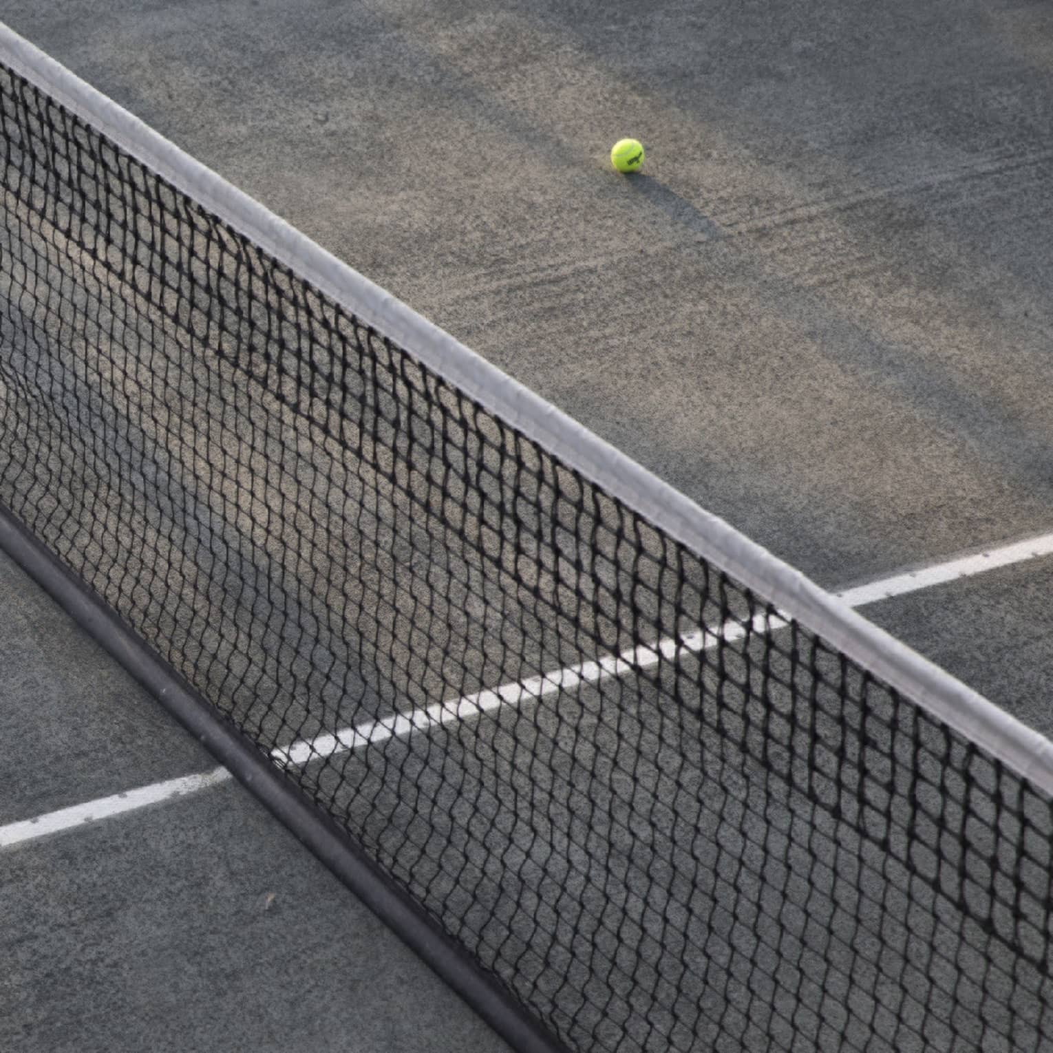 A lone tennis ball lies near the net on an empty court