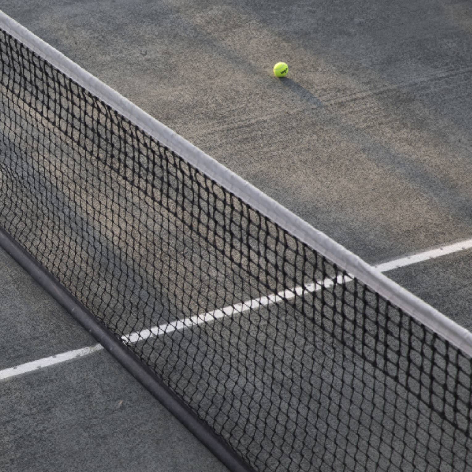 A lone tennis ball lies near the net on an empty court