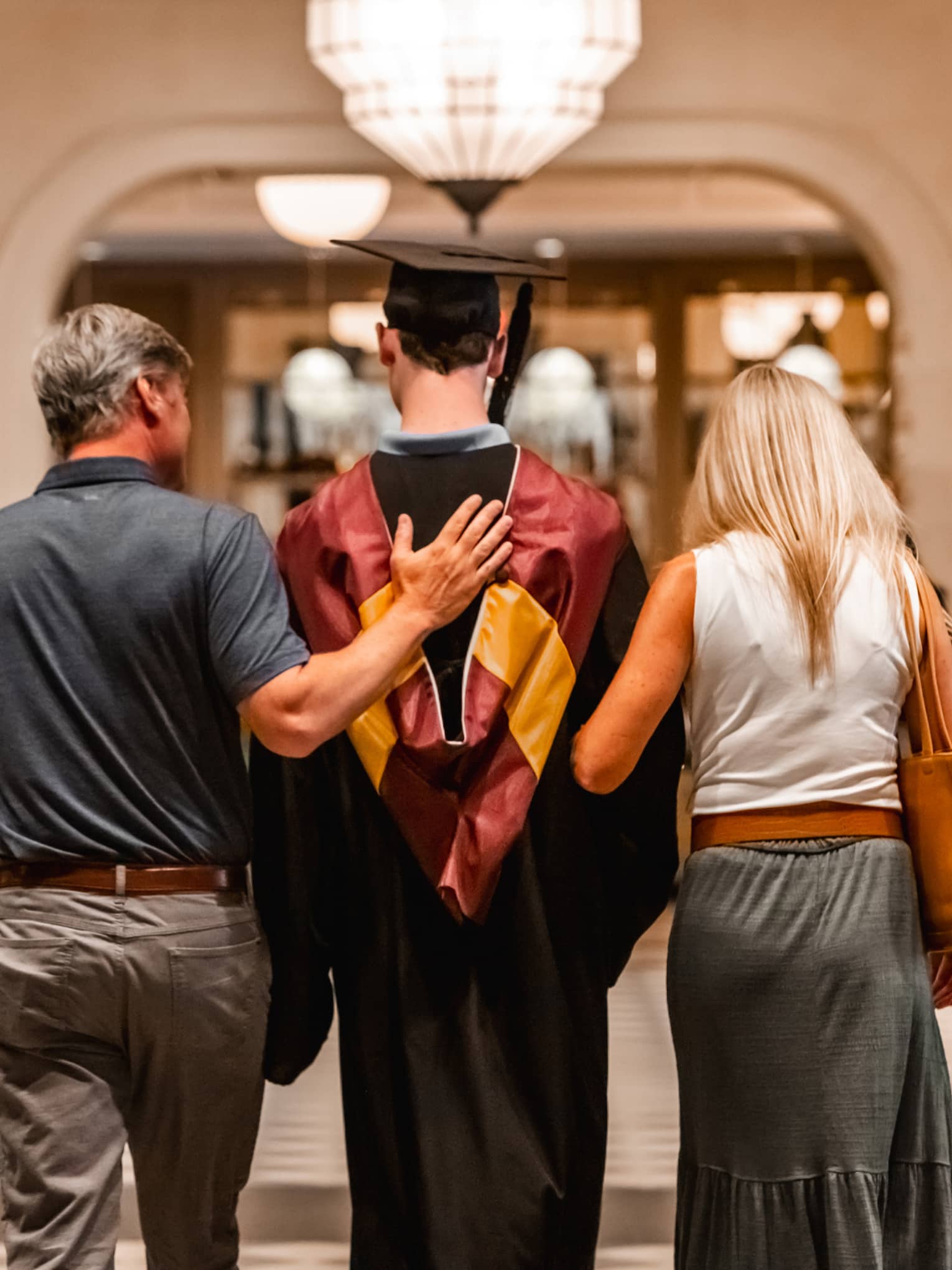 Parents walking with child in graduation gown.