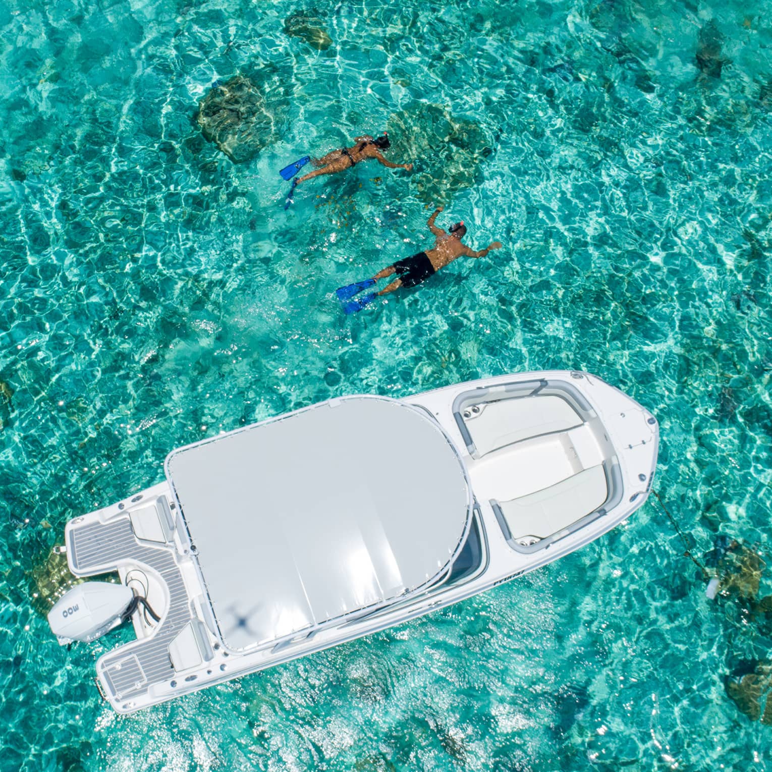 Two people swim alongside a boat in clear turquoise waters