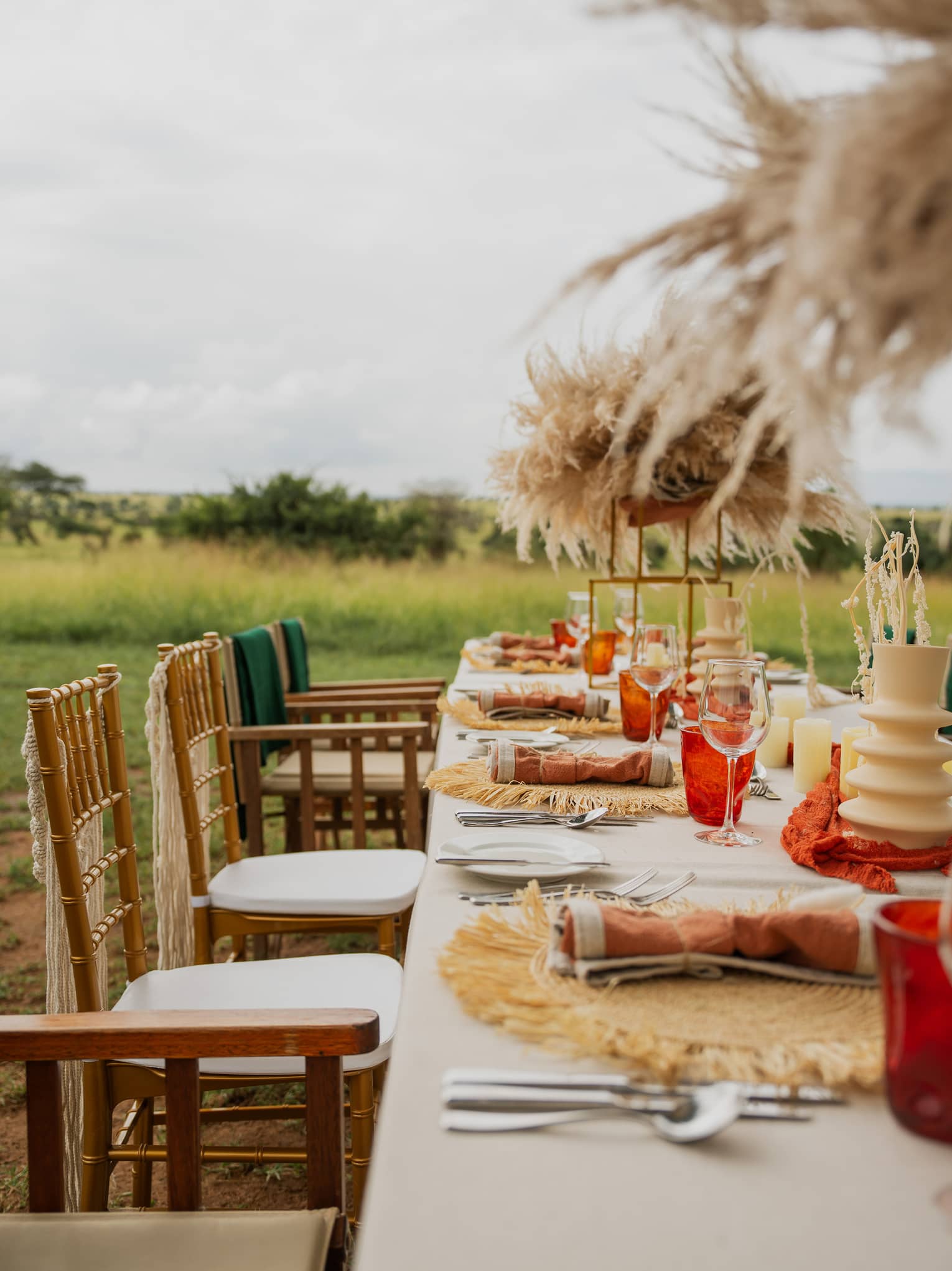 Long banquet table set with green and orange d�cor and natural grass arrangements on a plain