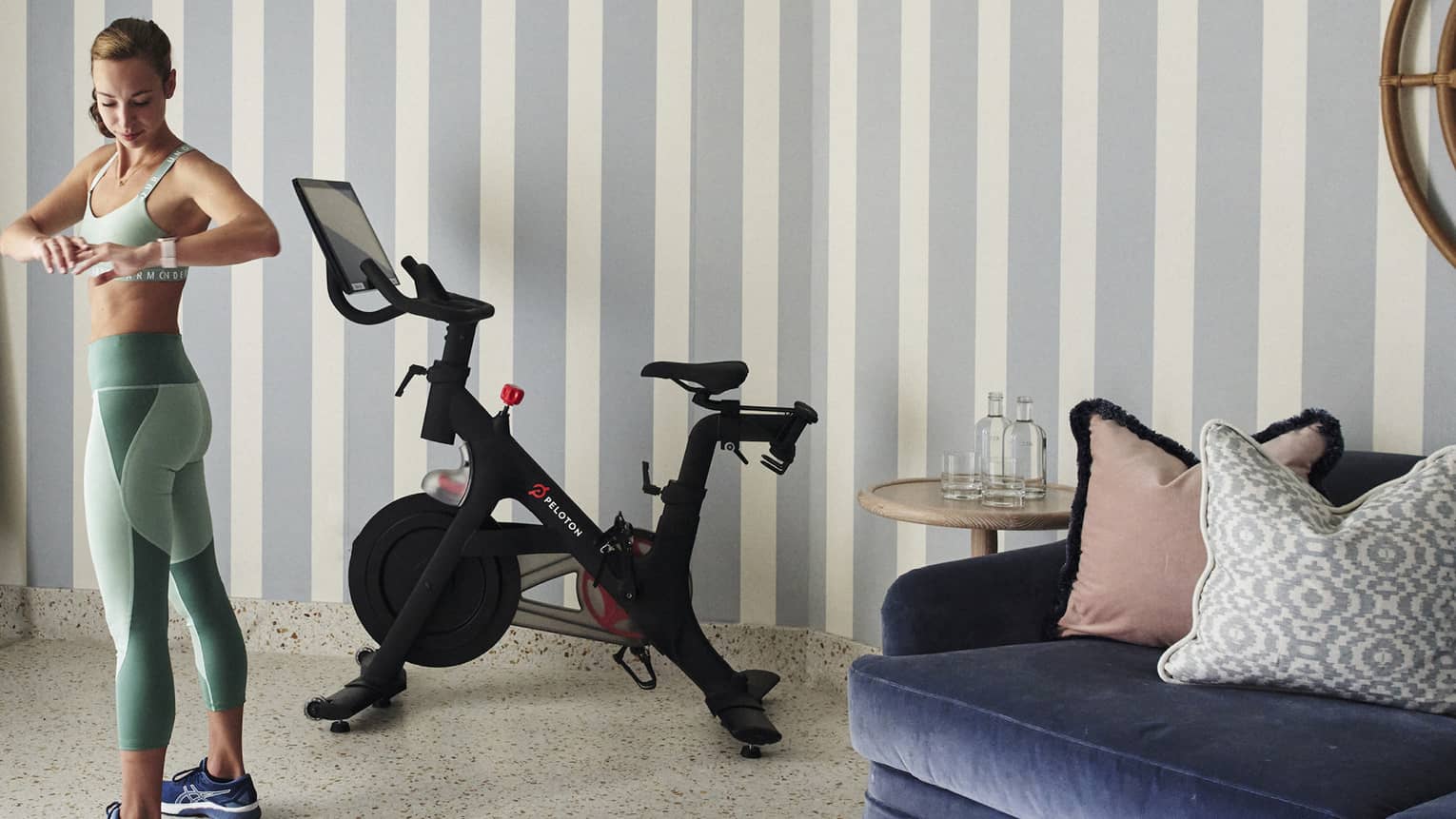 A woman in workout clothes in a hotel room with a stationary bike.