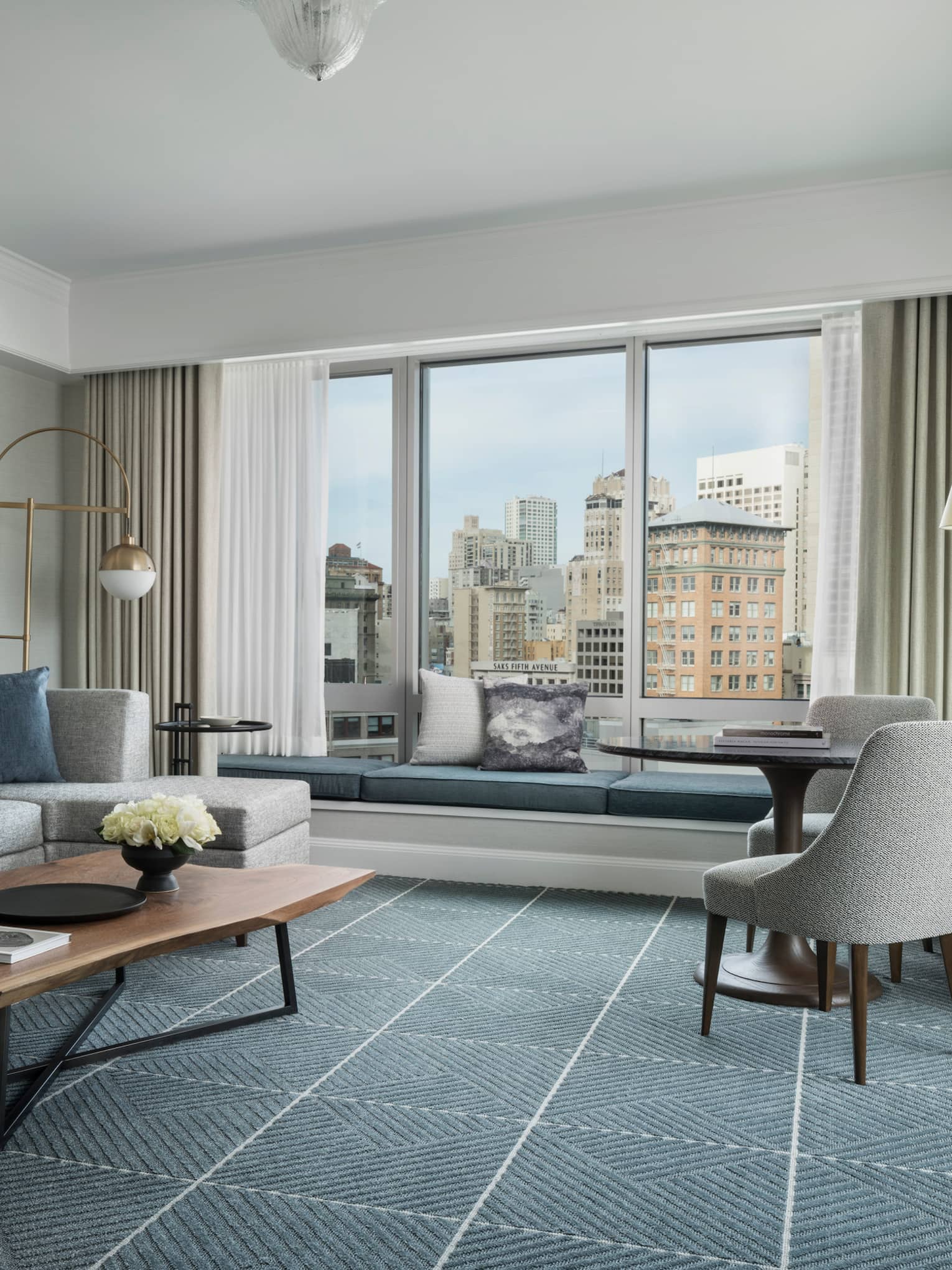 Hotel room with modern seating area, grey sofa by large window with padded bench