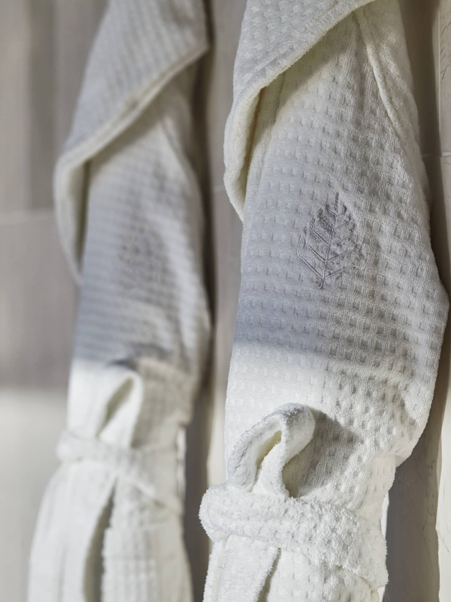 Two spa robes hanging on a wall of smooth tile.