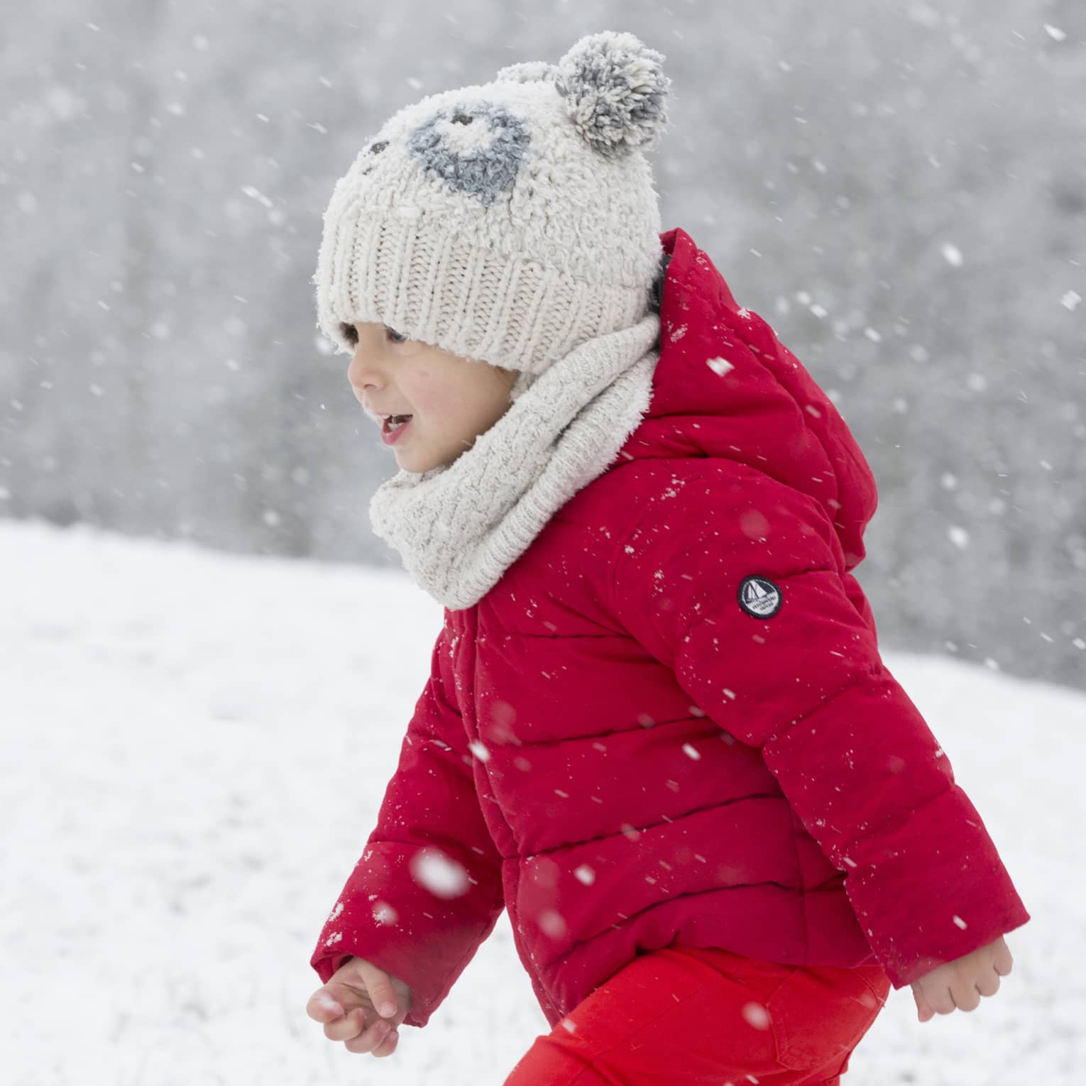 Child wearing red snowsuit and white hat playing in snow