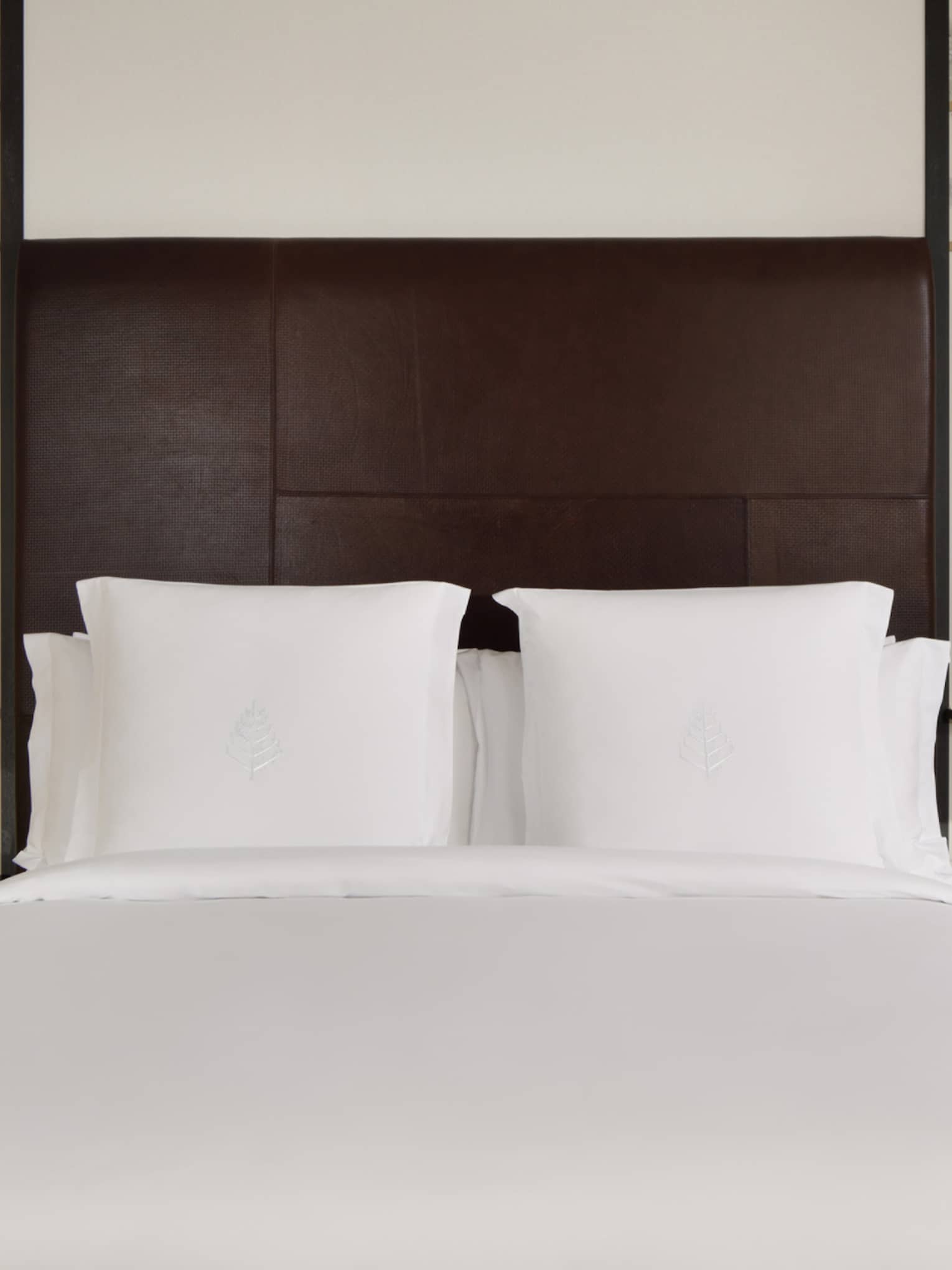 Deluxe guest room with king bed, brown headboard, decorative floral wall panels and bedside tables with a lantern lamp and flower vase