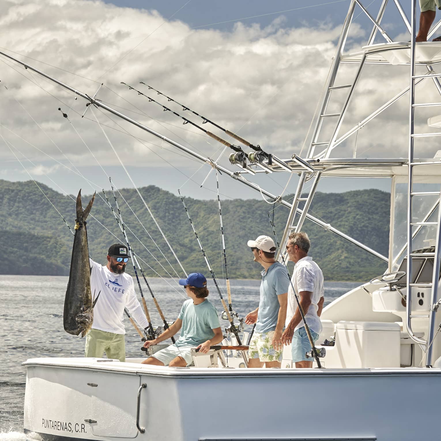 Four men are gathered on the back of a fishing boat with one of them holding a large fish up by the tail