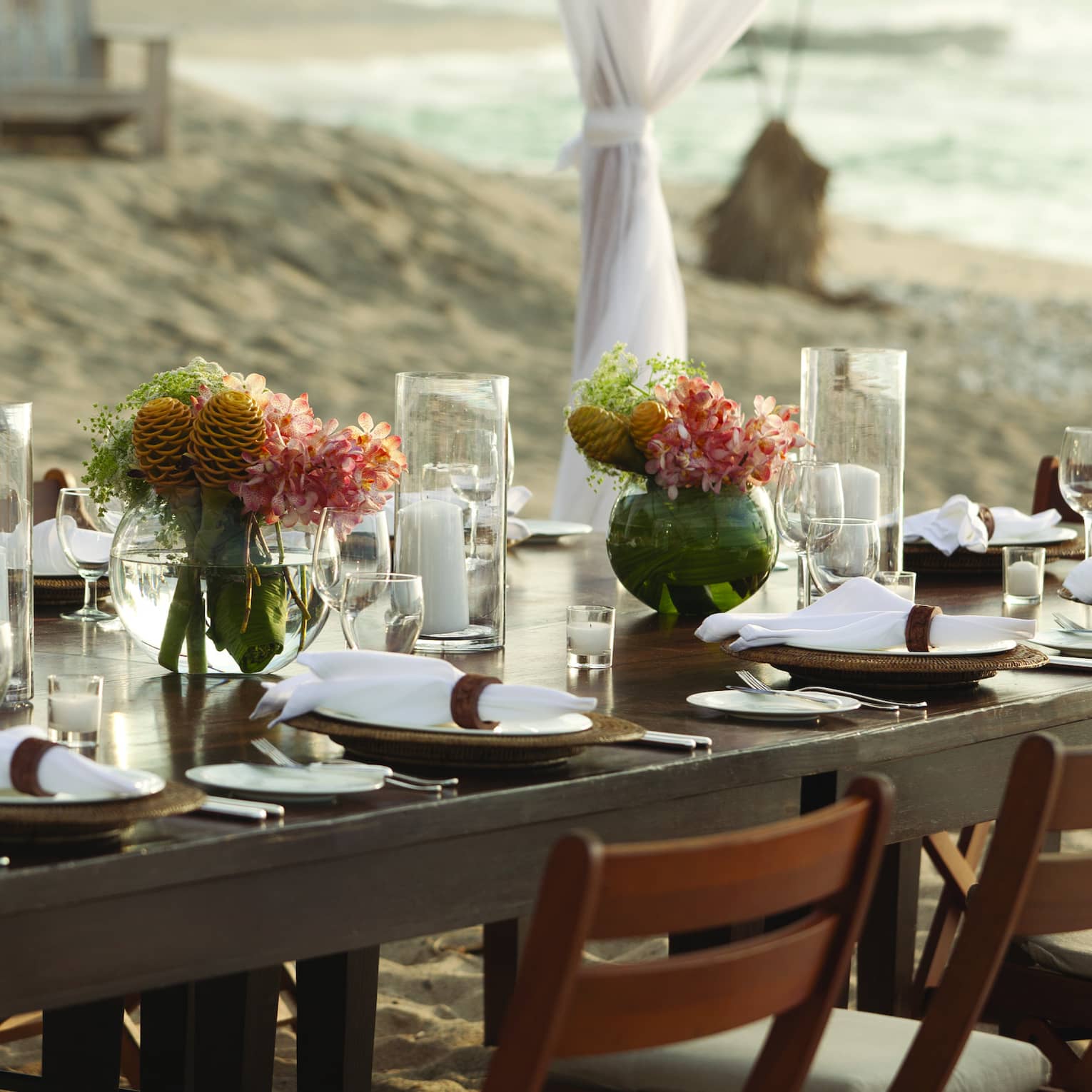Close-up of private dining table with flowers, candles under sheer white linen drapes on beach