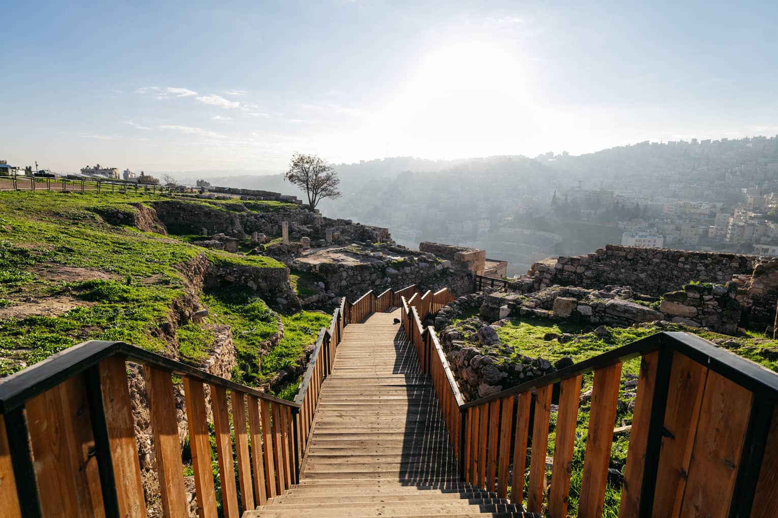 Long wooden walkway leads from a rocky hilltop down to a city below