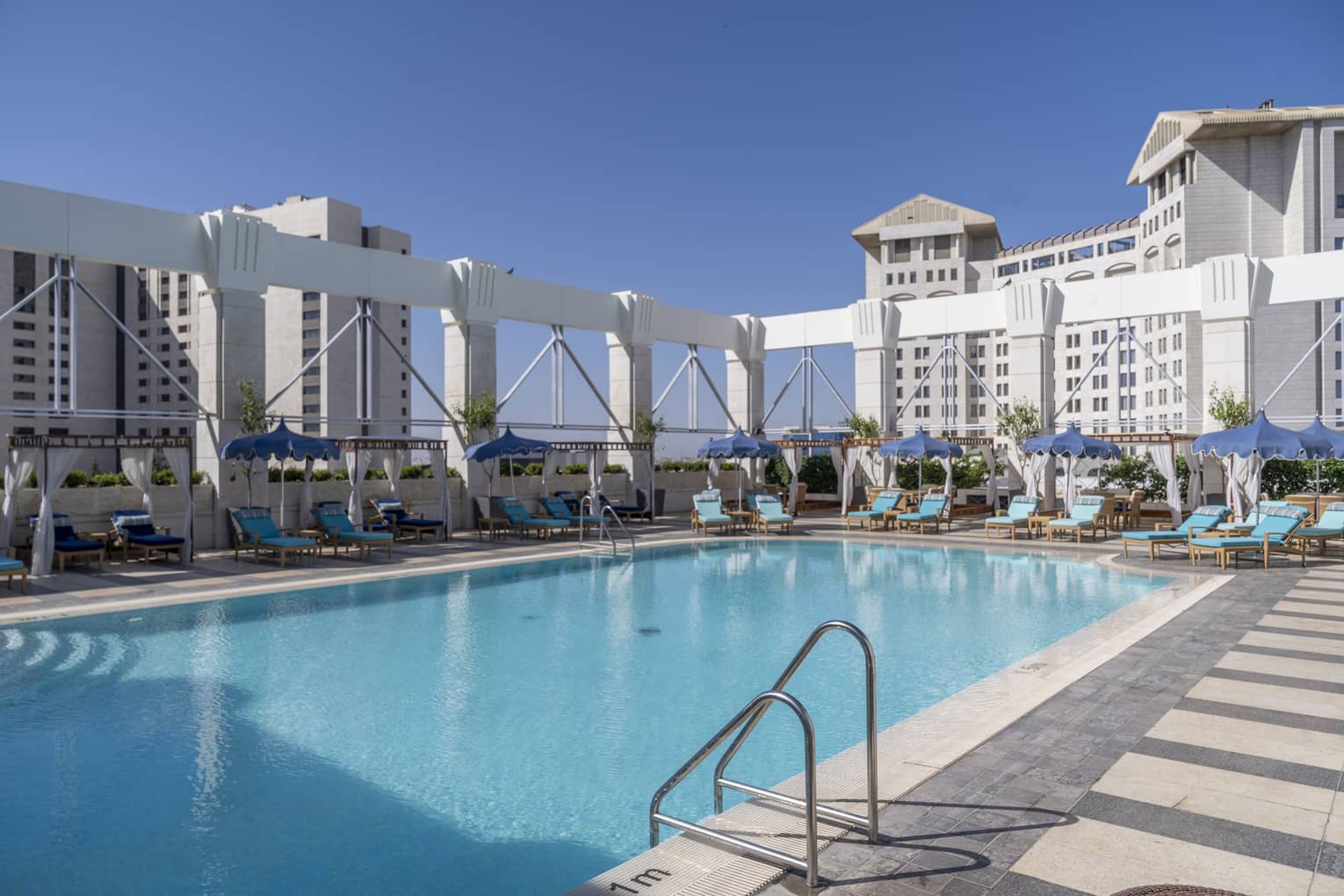 Outdoor pool surrounded by teal lounge chairs and white column