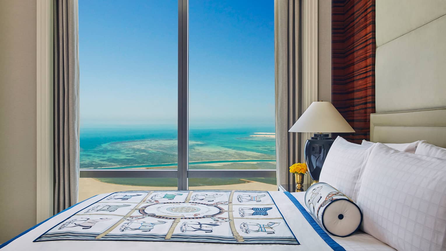 Premier Room top side view of bed with decorative blanket in front of floor-to-ceiling window with Arabian Gulf view