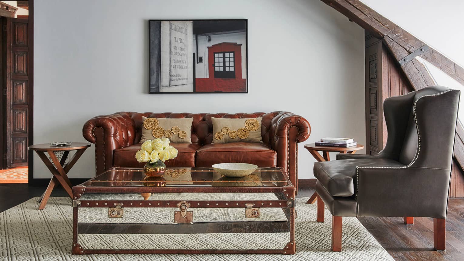 Trunk-style coffee table in front of period-style brown leather sofa, modern black armchair, oil painting