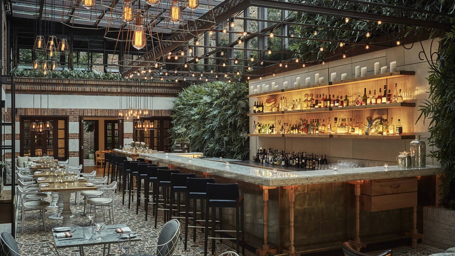 Castanyoles loft-style dining room under skylight and hanging lamps, long illuminated bar, green plants