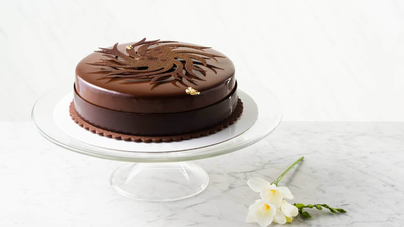 Round Gresham signature chocolate cake on glass cake plate and daffodils on table