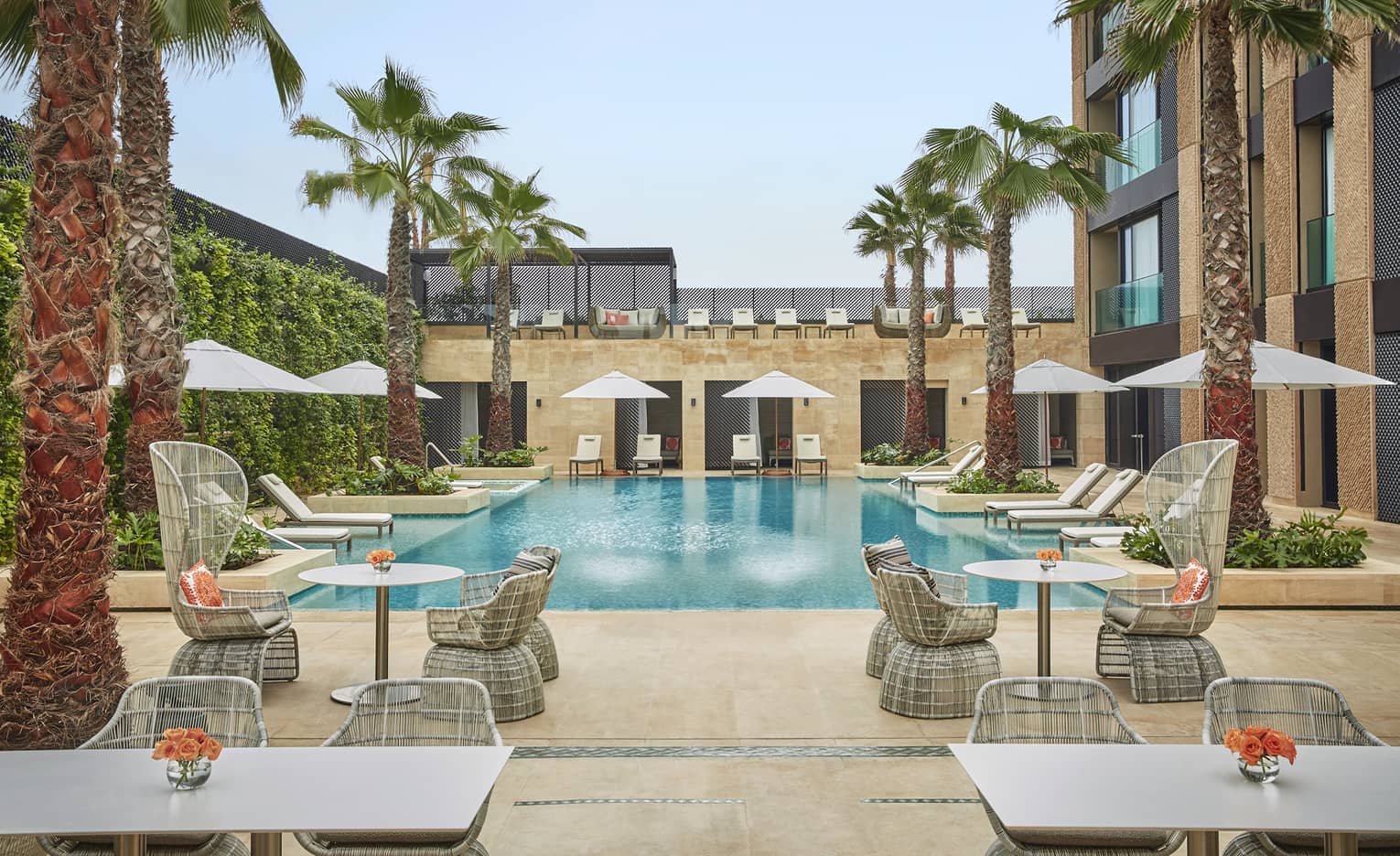 Courtyard pool flanked by tables and chairs with umbrellas, palm trees