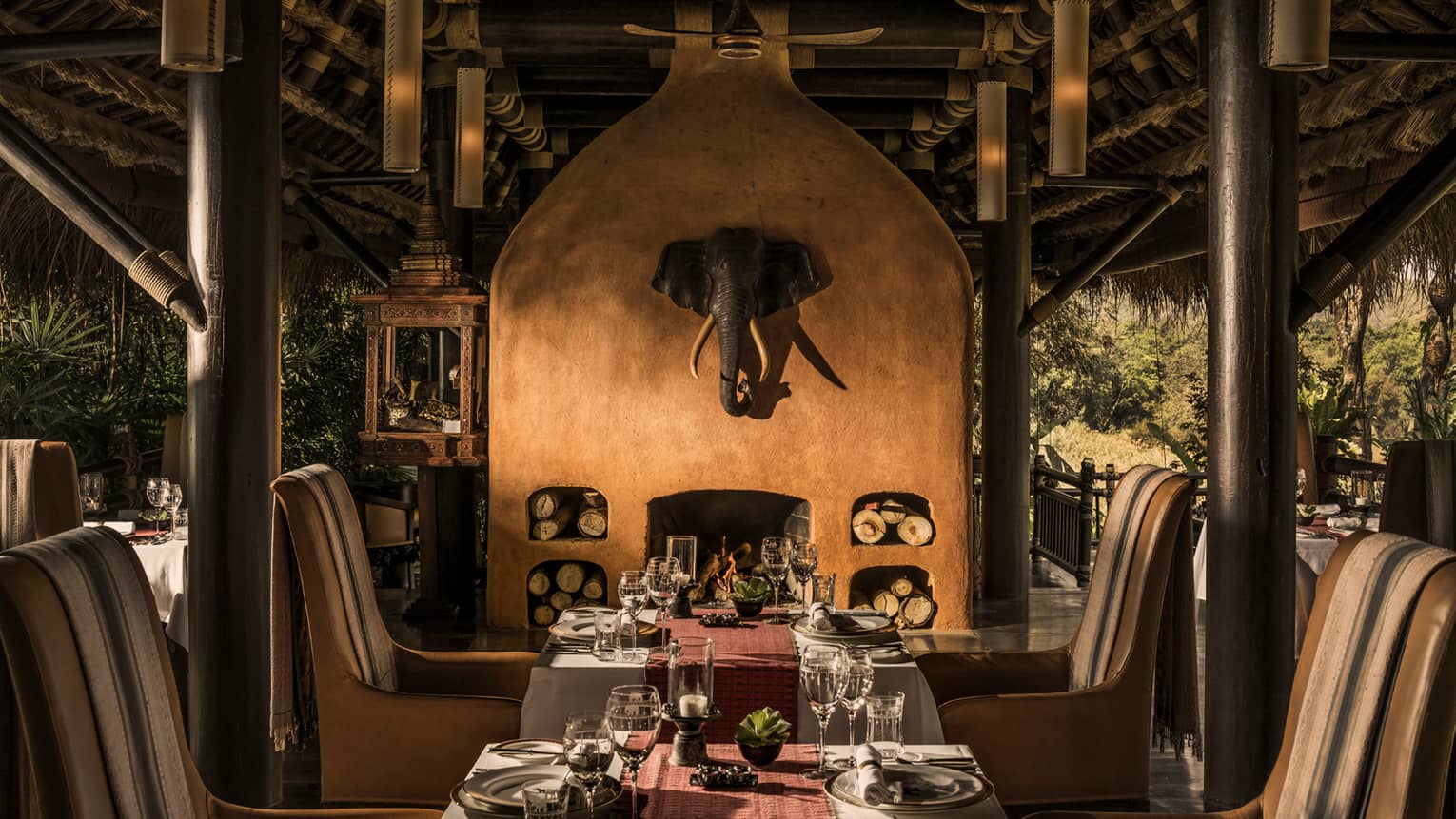 Dining tables in front of tall clay fireplace with mounted elephant head statue