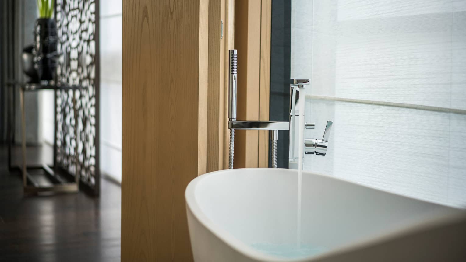 Water pours from faucet into modern freestanding white tub in large Studio Suite Burj Khalifa View room bathroom