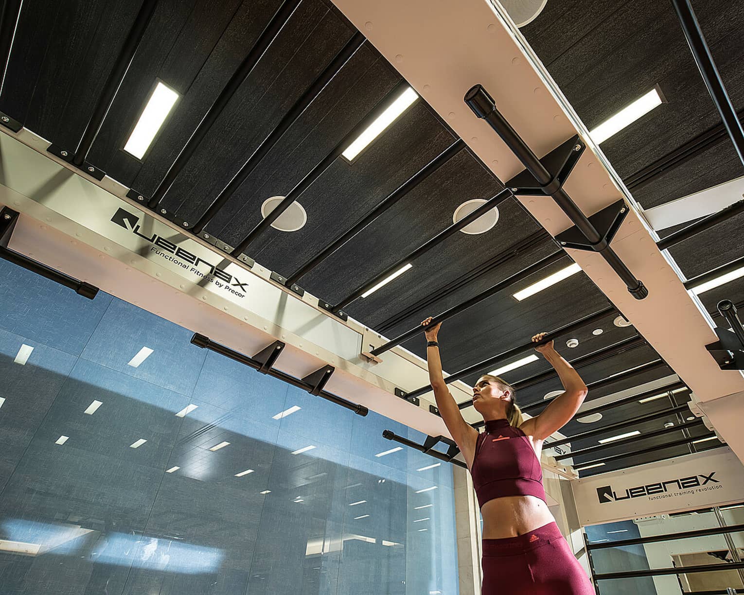 Person wearing two-piece burgundy workout outfit makes their way across a row of bars in a fitness centre