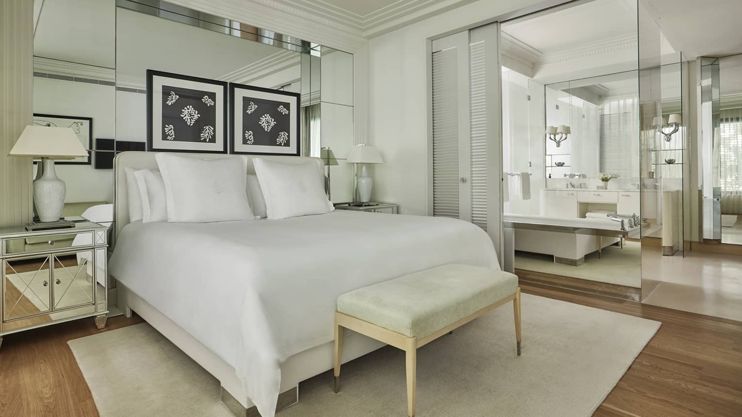 Hotel suite white bed against mirrored wall with green foot bench atop neutral rug 