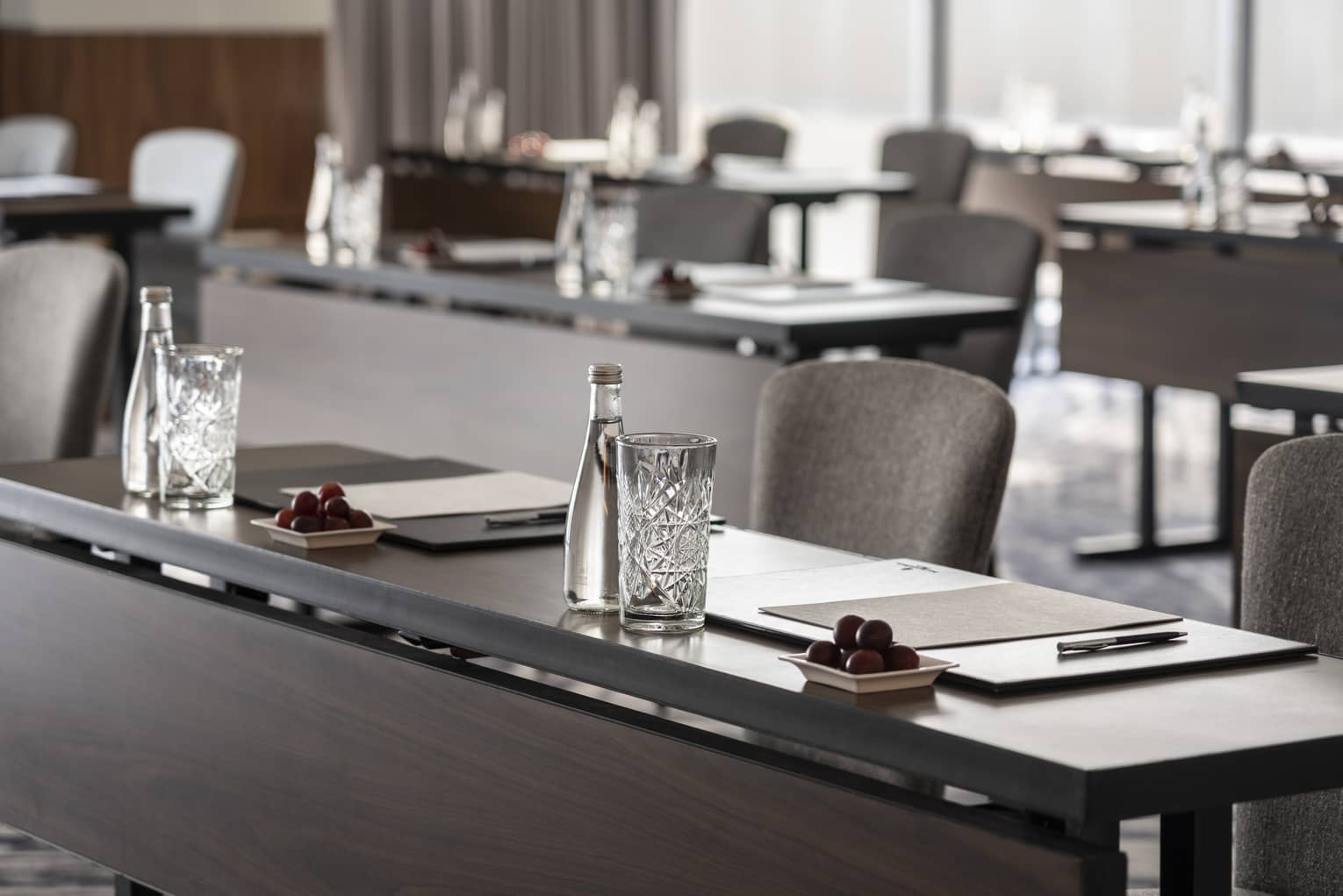 A close up of long desks with papers and water placed at each seat.