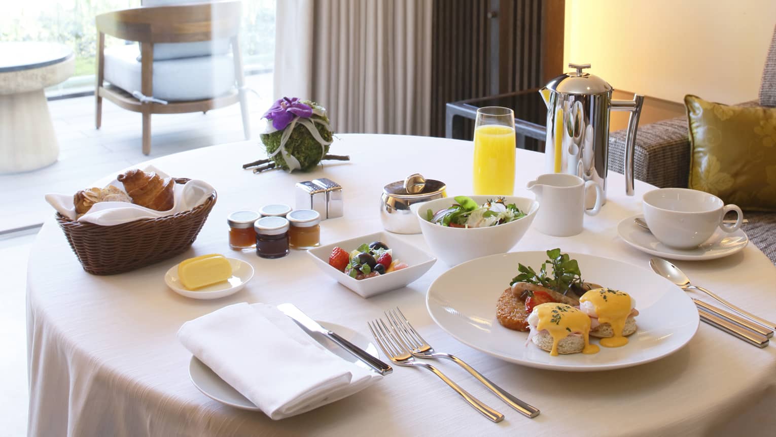 Eggs benedict brunch on plate, fruit and salad in bowls