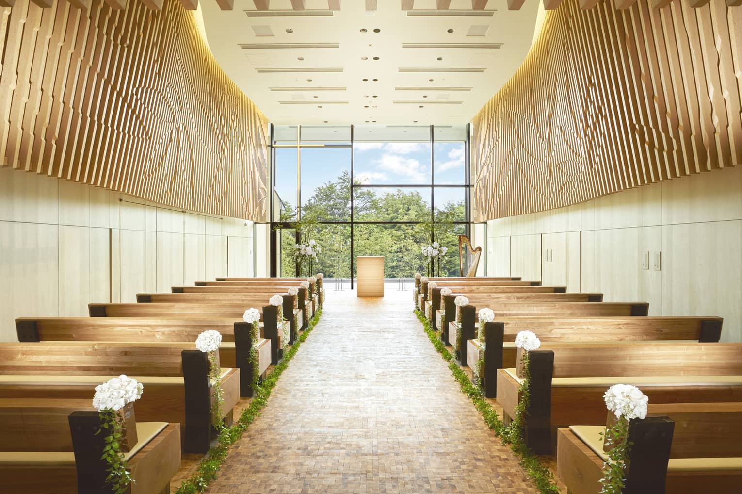 Rows of pews on either side of aisle, floor-to-ceiling window in in bright, modern chapel