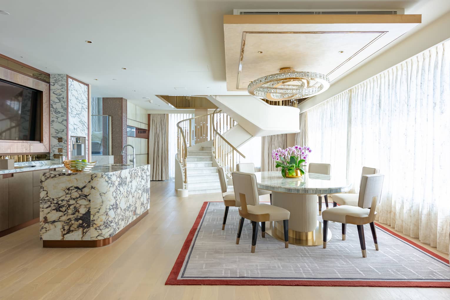 Dining area with round table and four chairs, chandelier, marble counter, spiral staircase in background