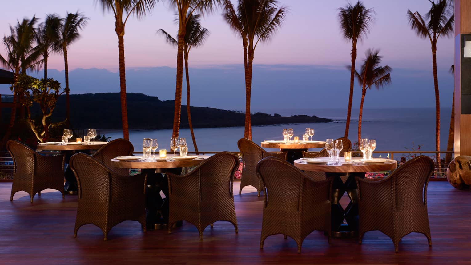 Wicker dining chairs around patio tables overlooking beach on One Forty patio at night