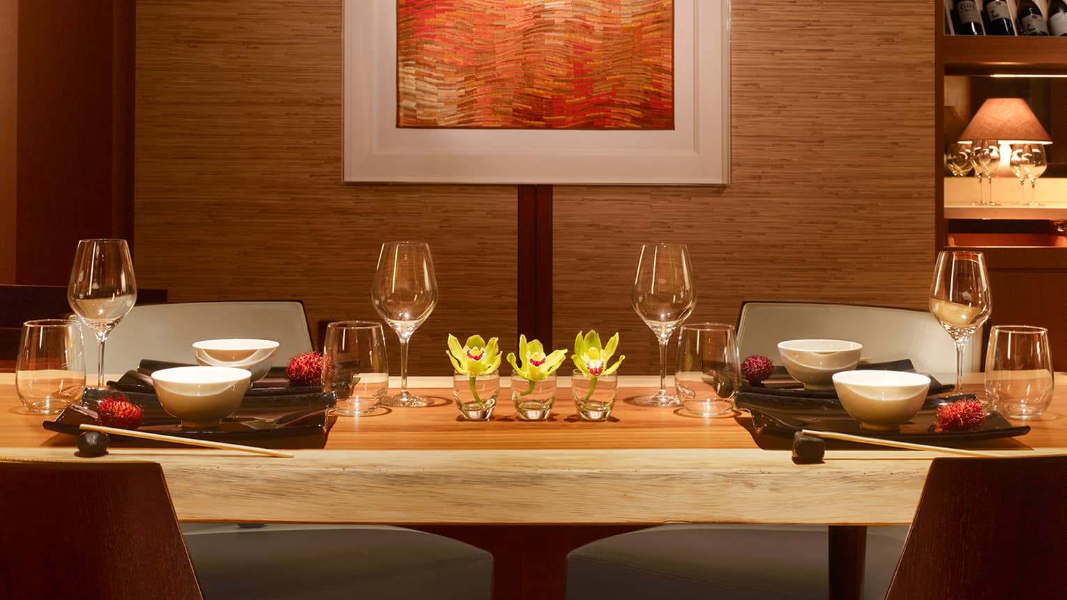 Long rustic wood private dining table with wine glasses, yellow flowers under wall with orange art 