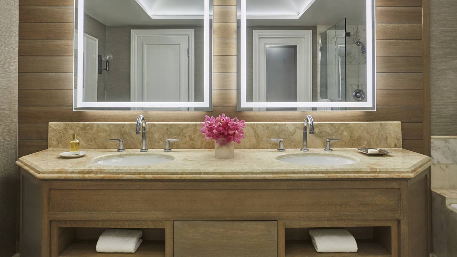 Bathroom vanity with dual sinks, marble countertop, pink flower arrangement and illuminated mirrors