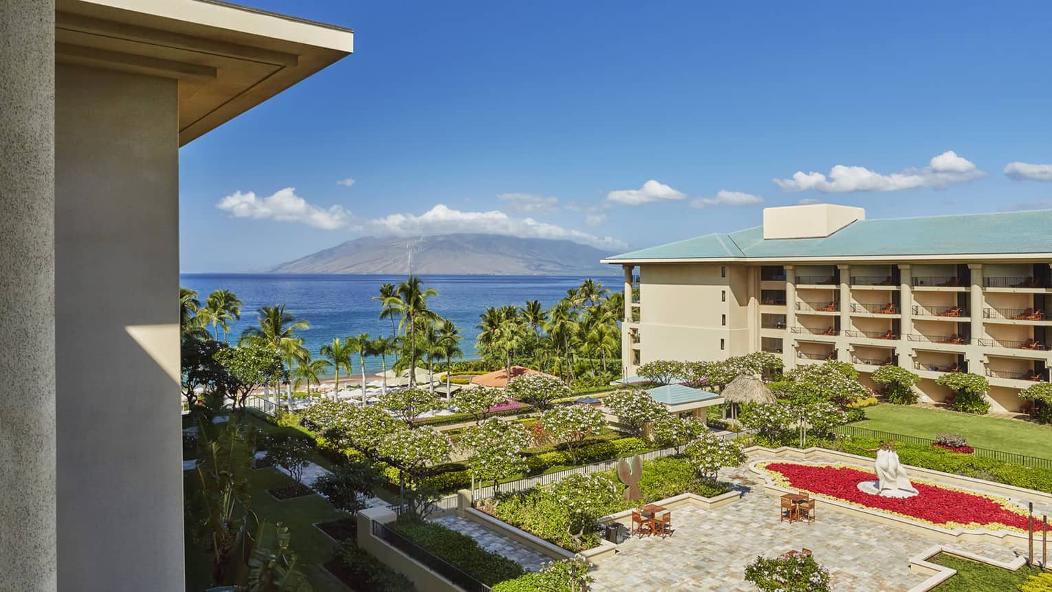 Luxury resort view with gardens, palm trees, ocean and distant mountain under a clear blue sky