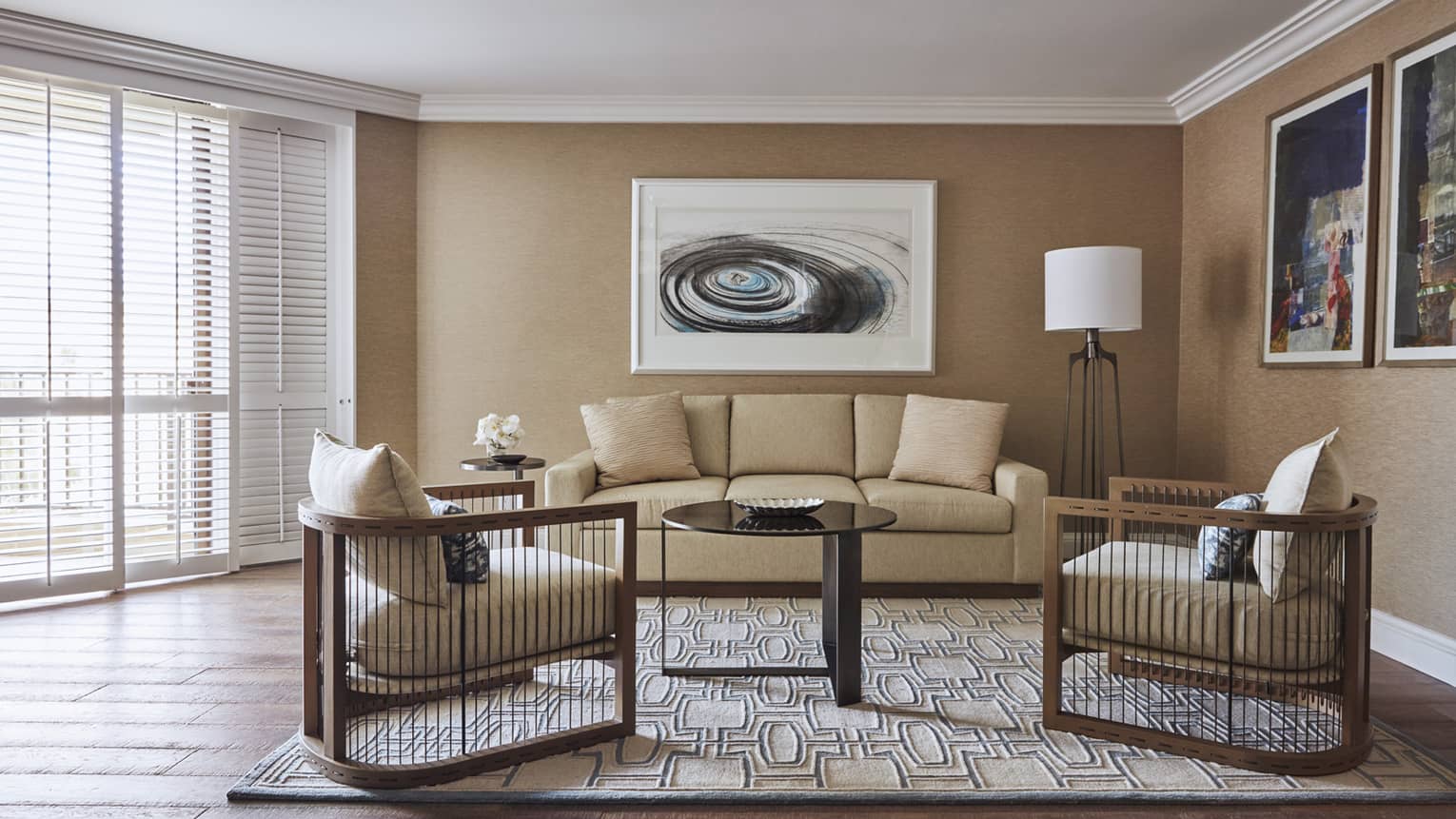 Living room with beige sofa, two wooden armchairs, abstract wall art, floor lamp and patterned rug