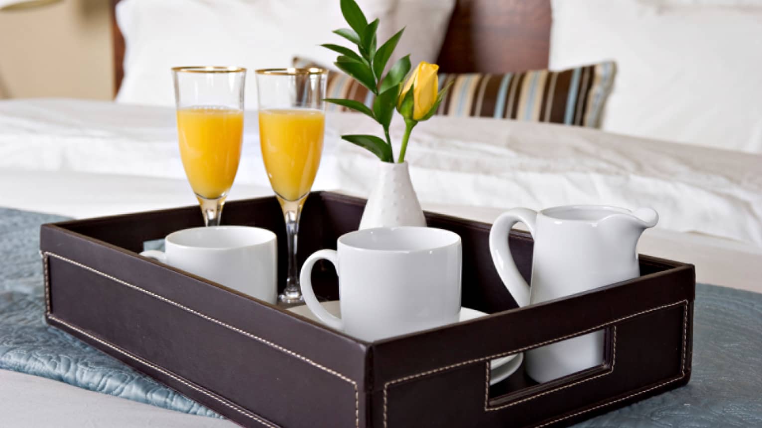 Close-up of in-room dining tray with two champagne and orange juice glasses, white coffee mugs, yellow flower