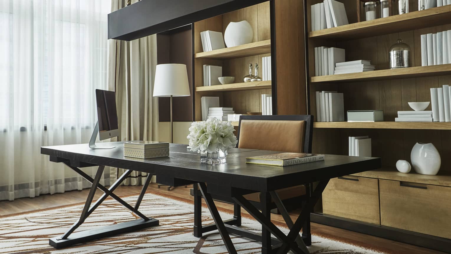 Elegant home office with a dark wood desk, leather chair, modern computer, and bookshelves adorned with minimalist decor and books, creating a calm and organized workspace.