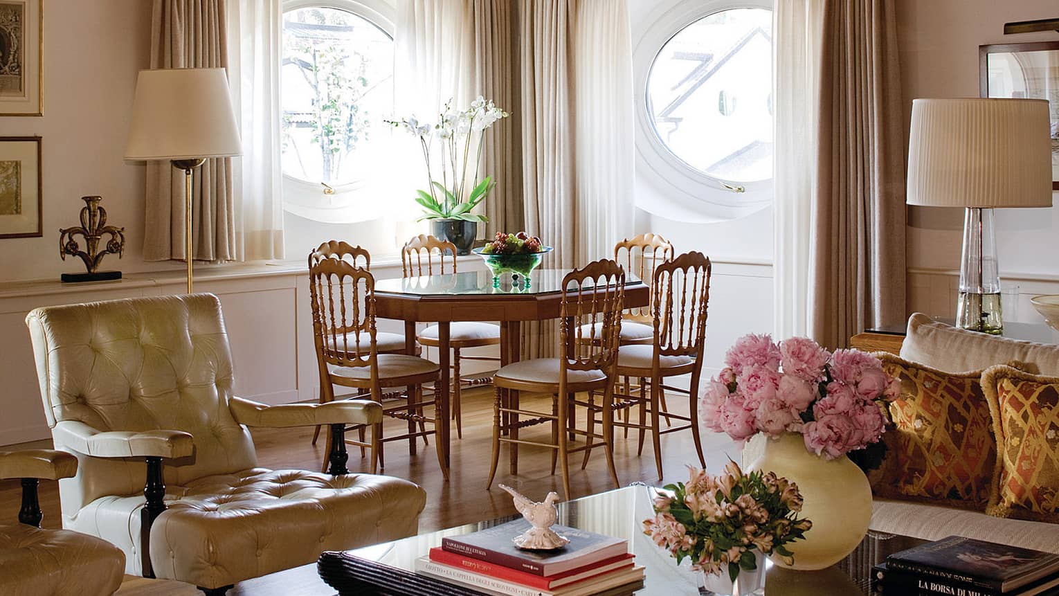 Hotel suite with neutral seating vignette around coffee table with flowers and books, wood dining table and chairs in backdrop