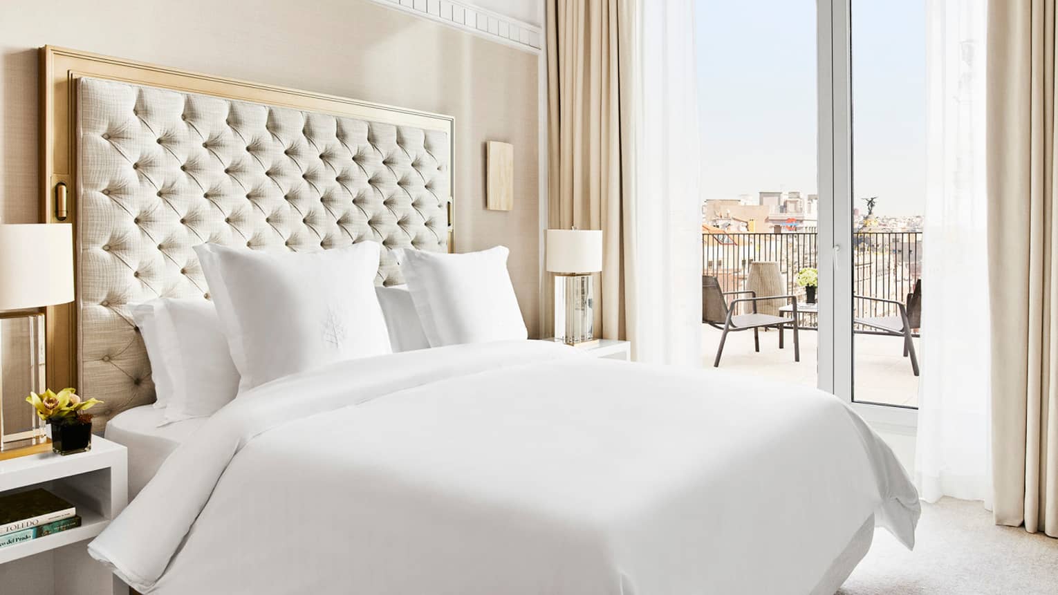 Luxury hotel suite bedroom with a king bed, tufted headboard, bedside lamps and access to a private terrace with city views