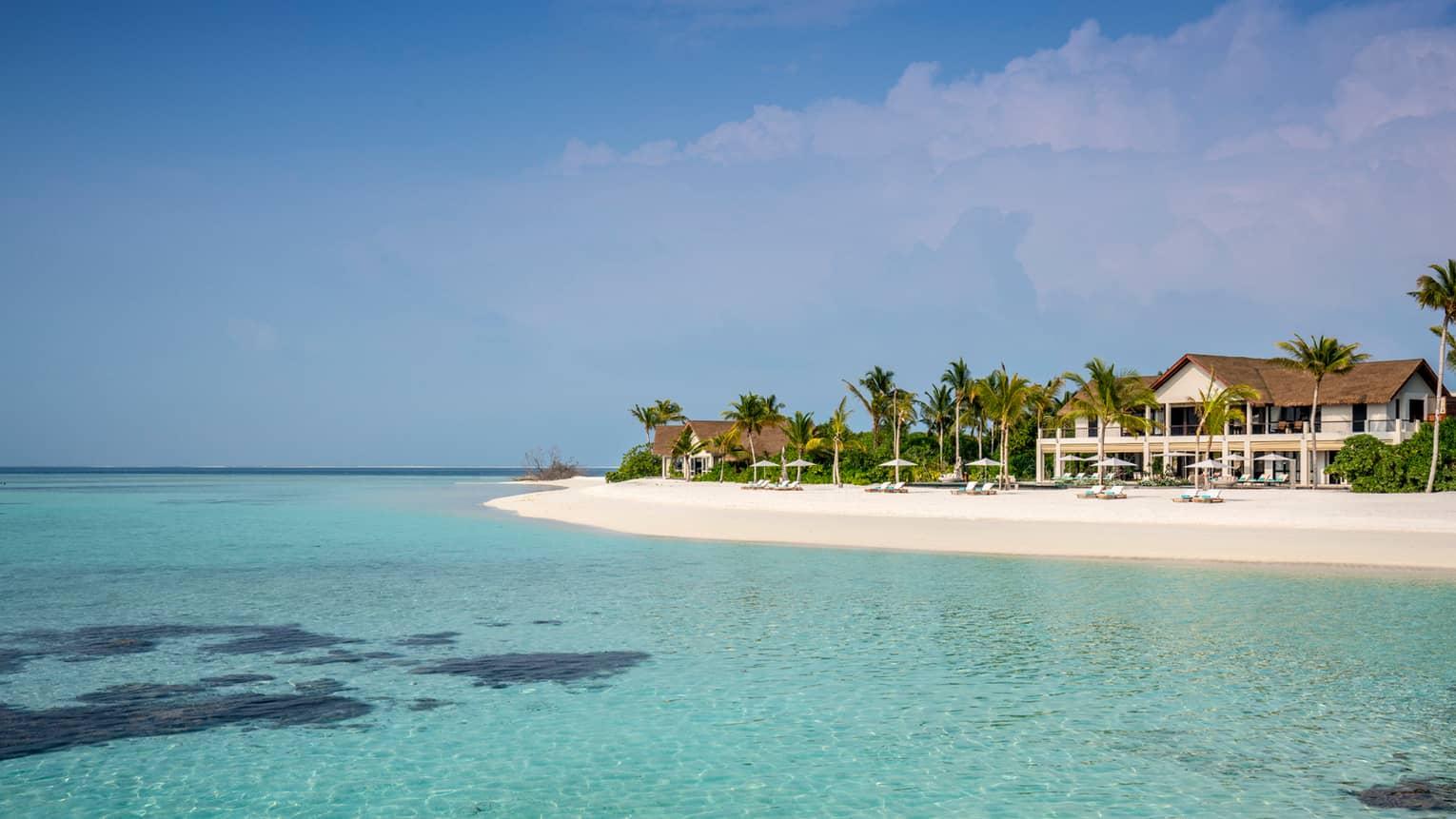 The Beach House building behind lounge chairs, umbrellas on private sand beach, turquoise lagoon