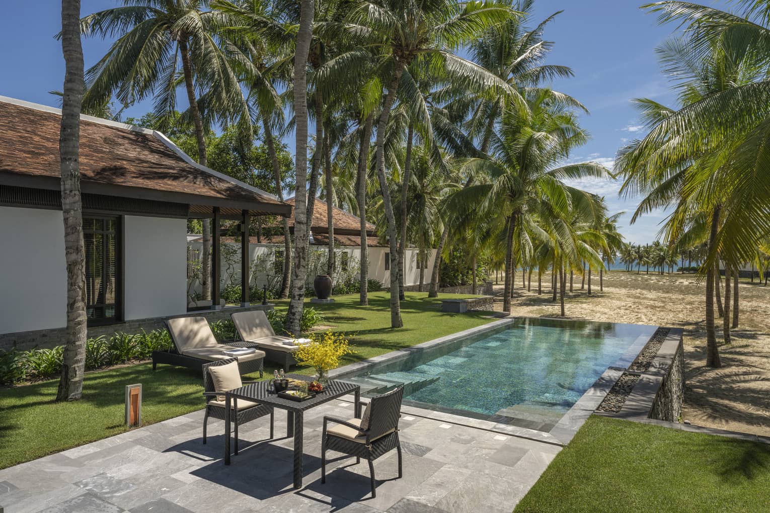 One Bedroom Pool Villa pool area with lounge chairs, two-seater table, palm trees and sunshine