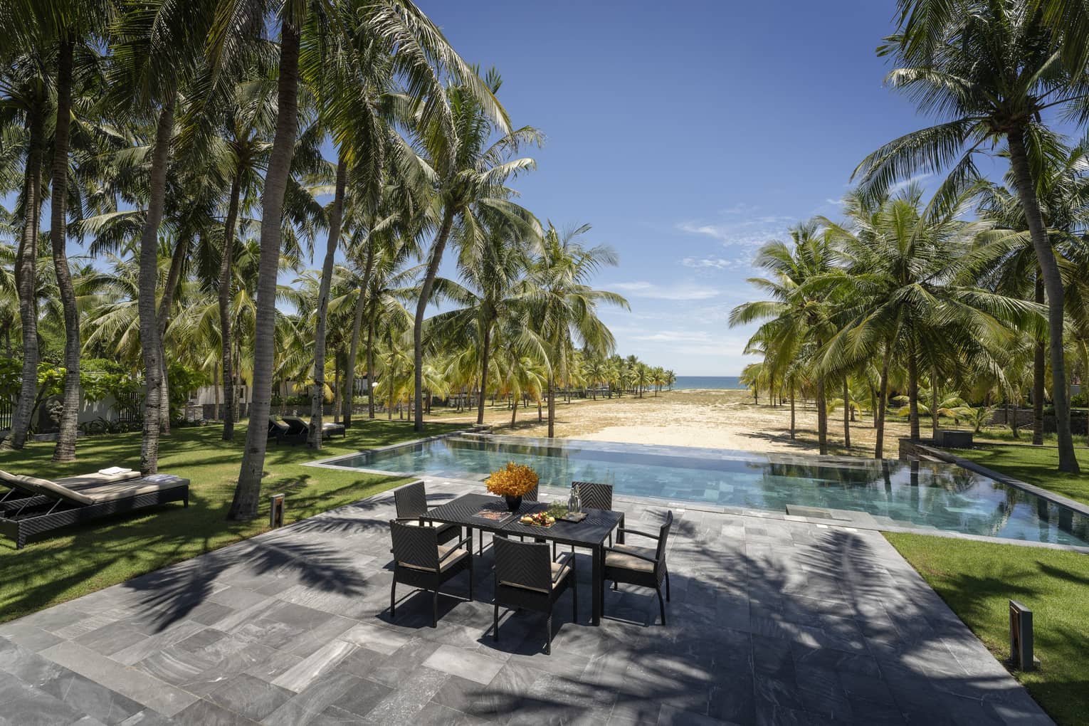 Three-Bedroom Pool Villa pool area with dining table, lounge chairs, palm trees, ocean views