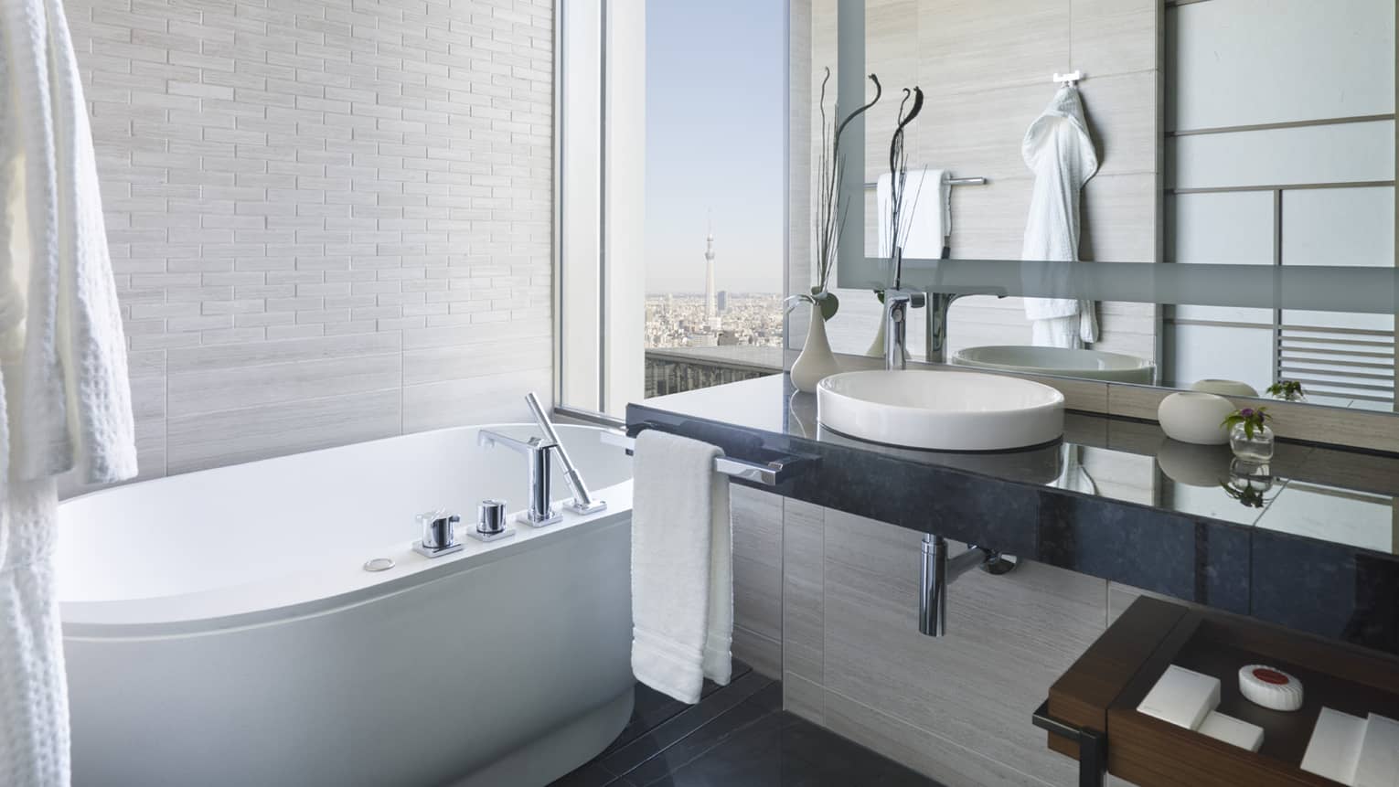 Bright bathroom with a freestanding bathtub, black granite vanity and large mirror, featuring a window with city views