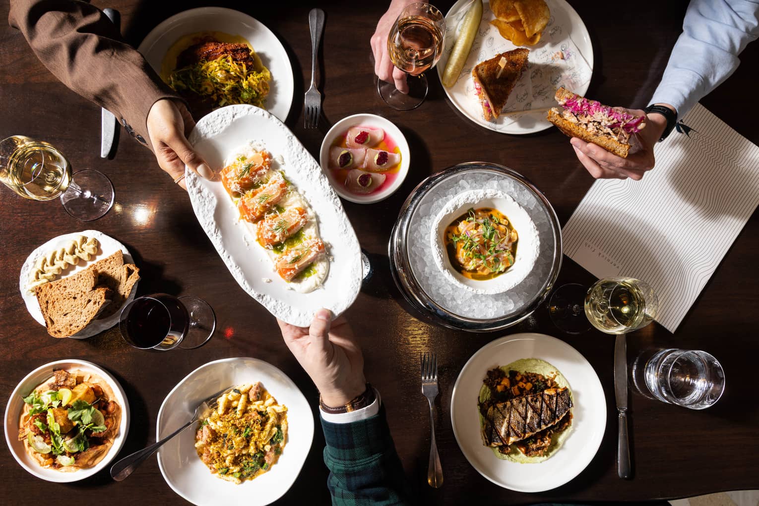 A dark wooden table topped with various colourful culinary dishes and glasses of wine