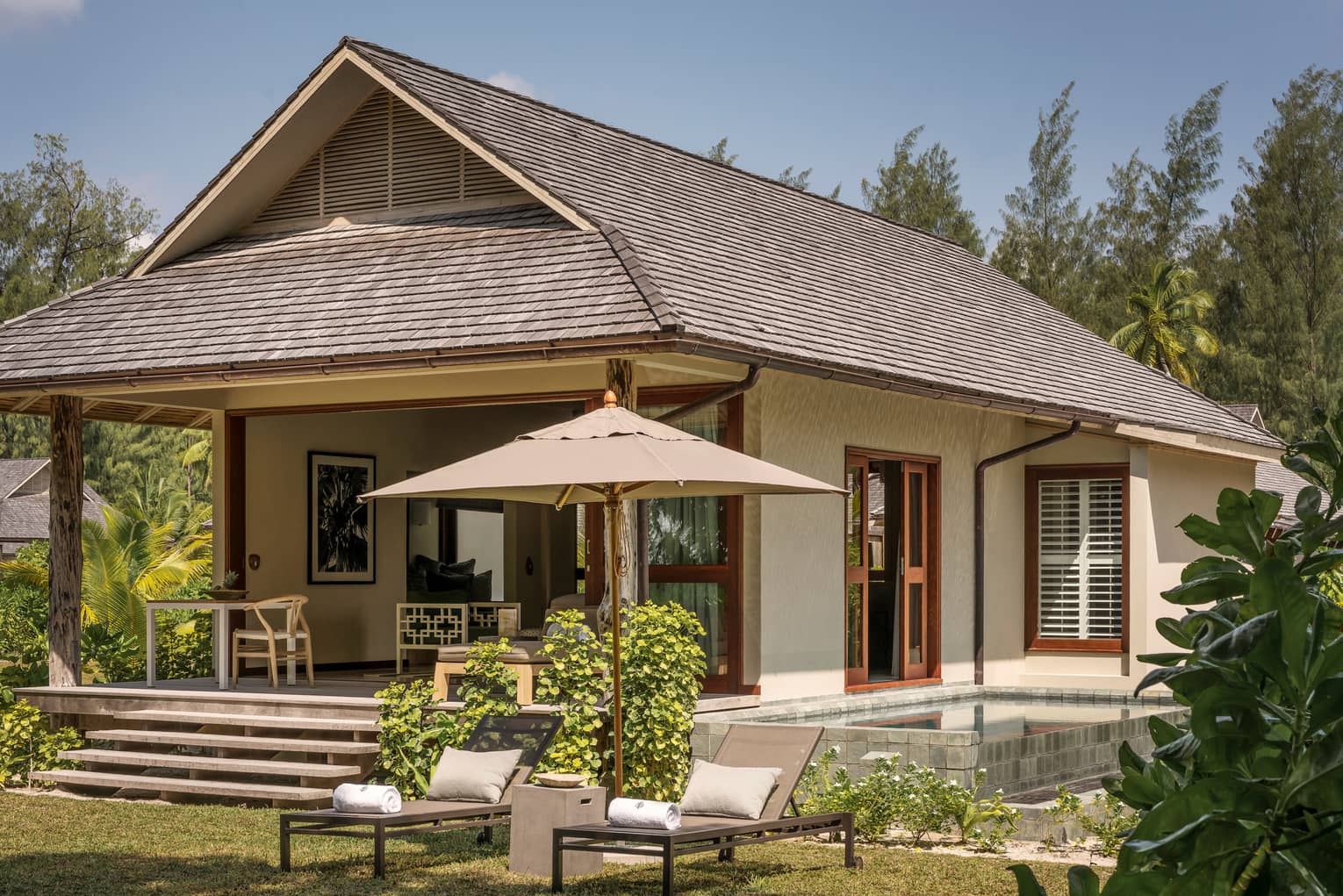 Exterior view of bungalow villa with two patio lounge chairs, umbrellas on lawn