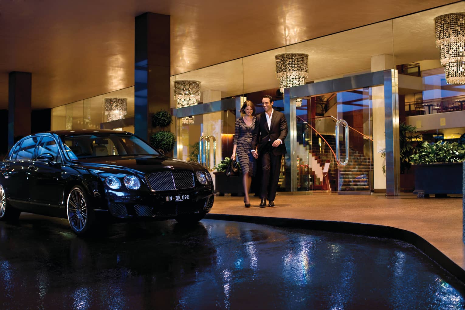 Man and woman walk arm-in-arm past luxury car, Four Seasons Hotel Sydney entrance