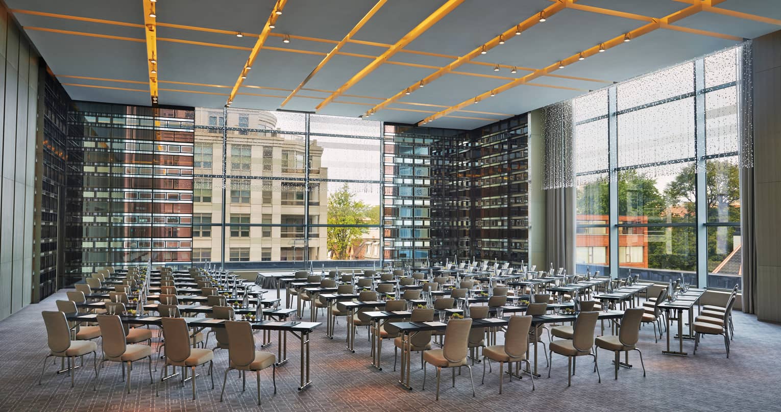 Chairs, tables set up in rows in glass room with corner windows 