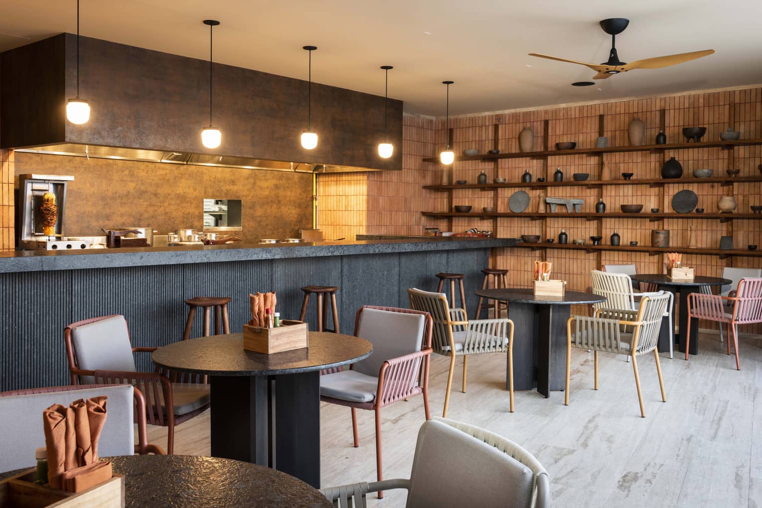 Hip restaurant with black round tables, colourful metal chairs and a bar with pendant lights