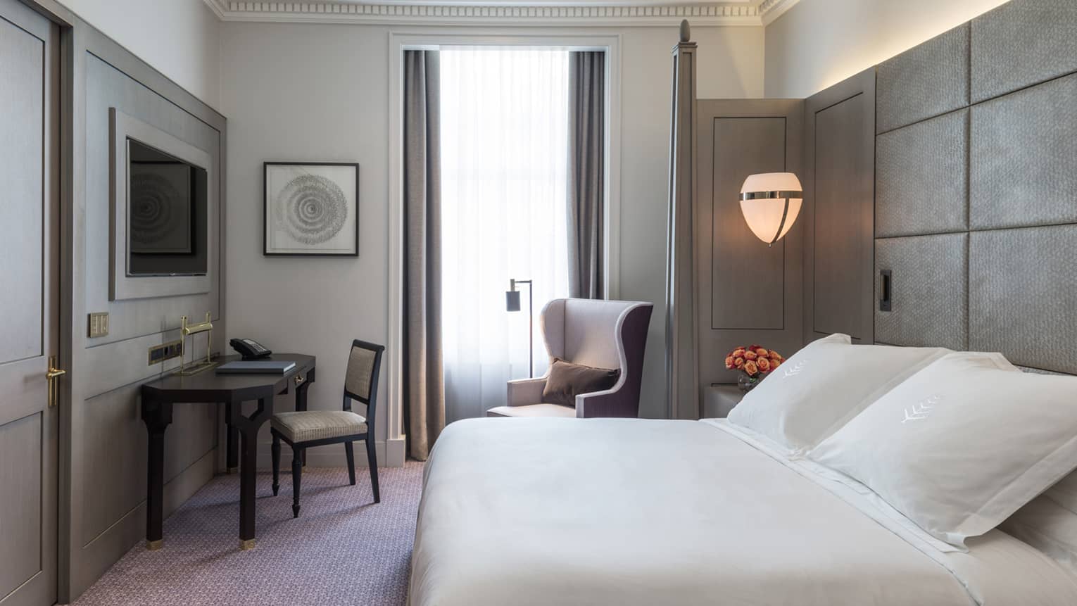 Superior room view with grey and white decor,  flat-screen tv above desk and reading chair and lamp by tall window