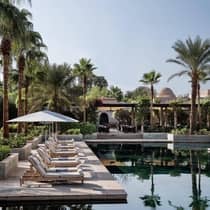 White lounge chairs, umbrellas line outdoor swimming pool surrounded by towering palm trees